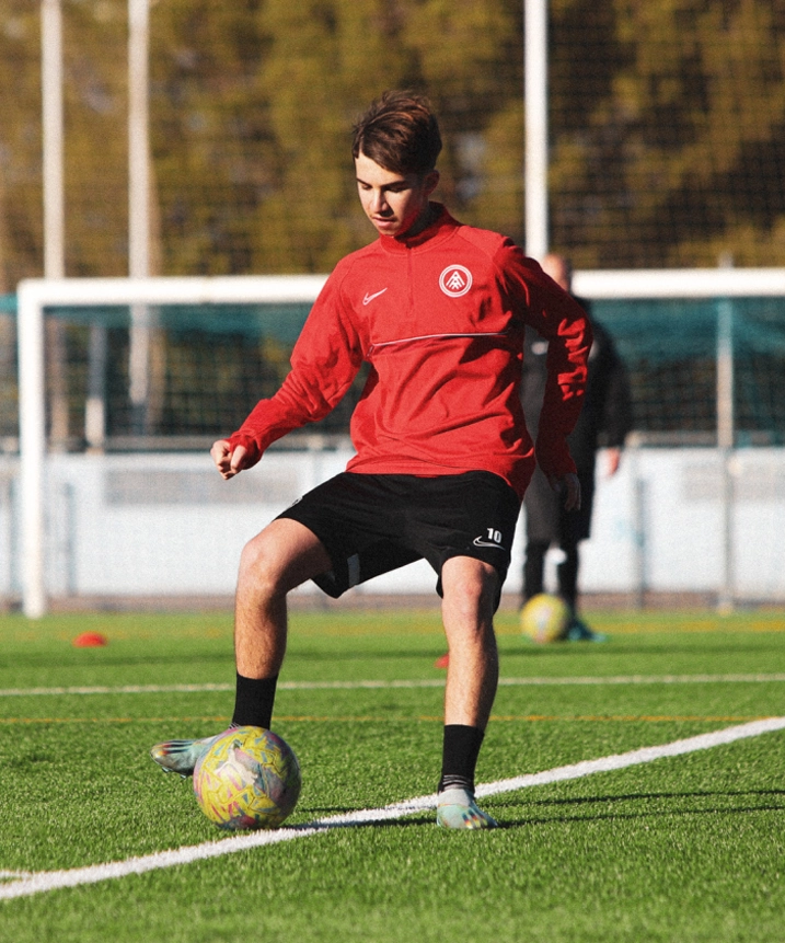 Jugador joven de fútbol en control del balón durante un entrenamiento, vestido con uniforme rojo y negro del Andorra.